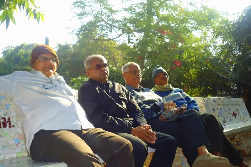 Four older friends sitting together on a garden bench in the sun