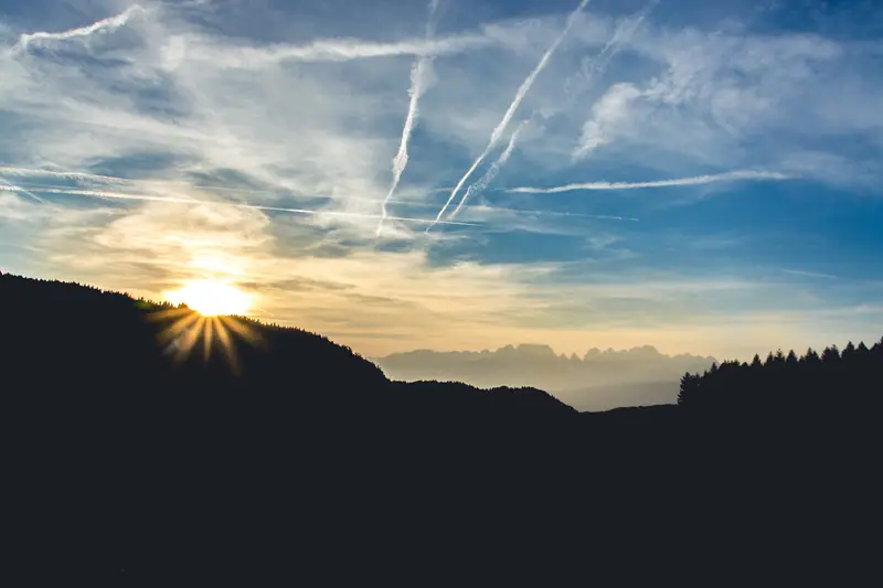 The sun rising over a hill under a streaked sky